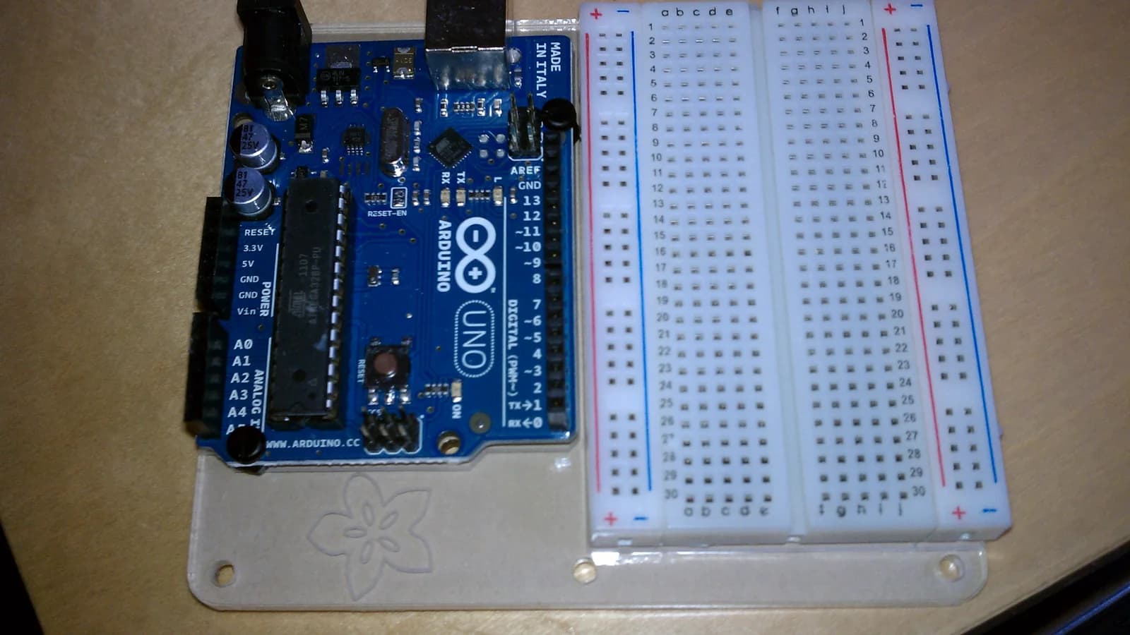 An Arduino board wired to a solderless breadboard on a white surface, with a short jumper lead between them.