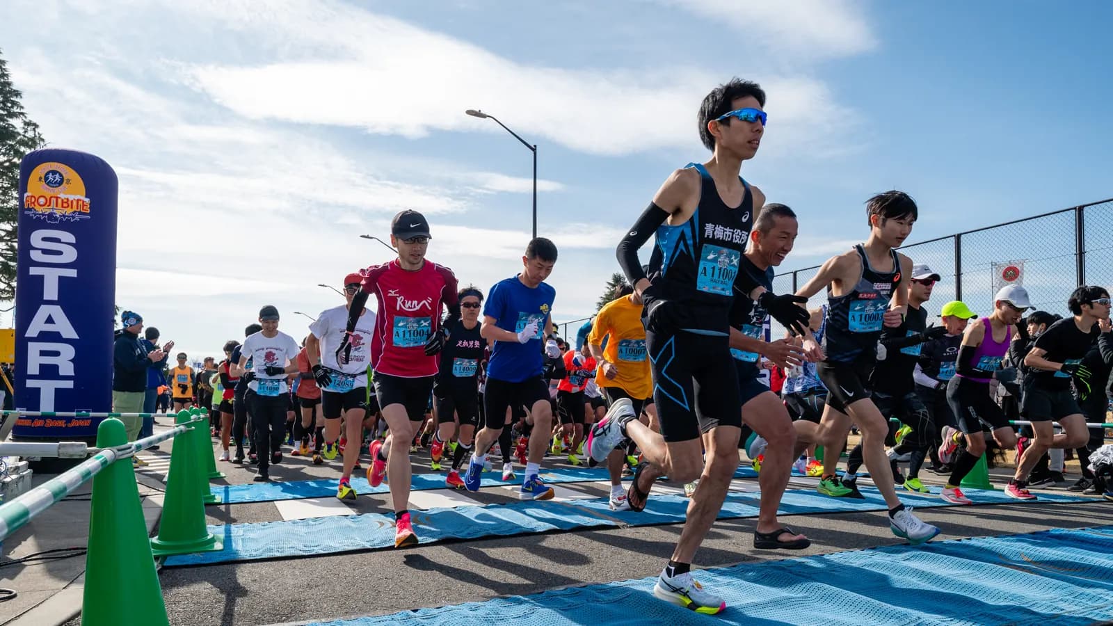 A dense field of runners crossing a timing mat under a start banner at the beginning of a road race.